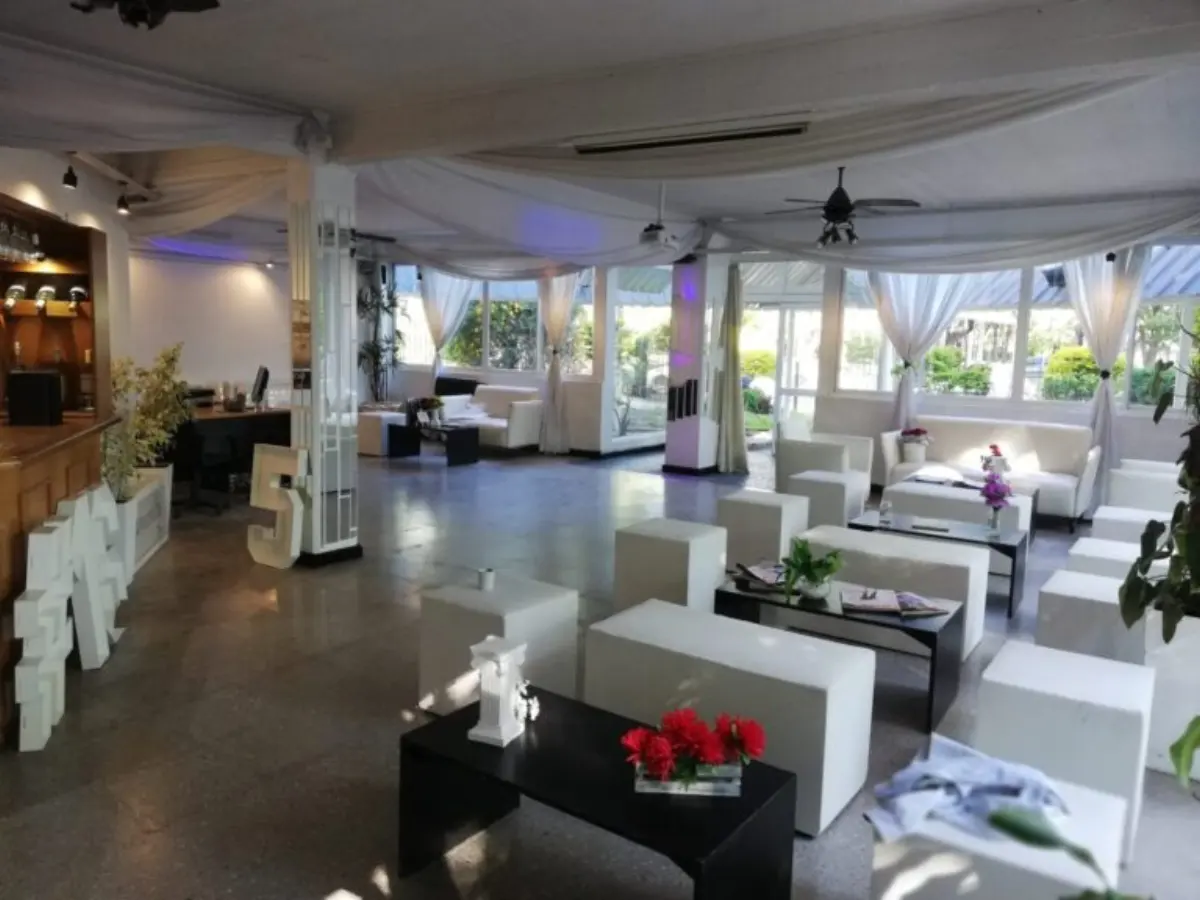Sector living cubierto con sillones blancos, cortinas y mesas bajas con flores