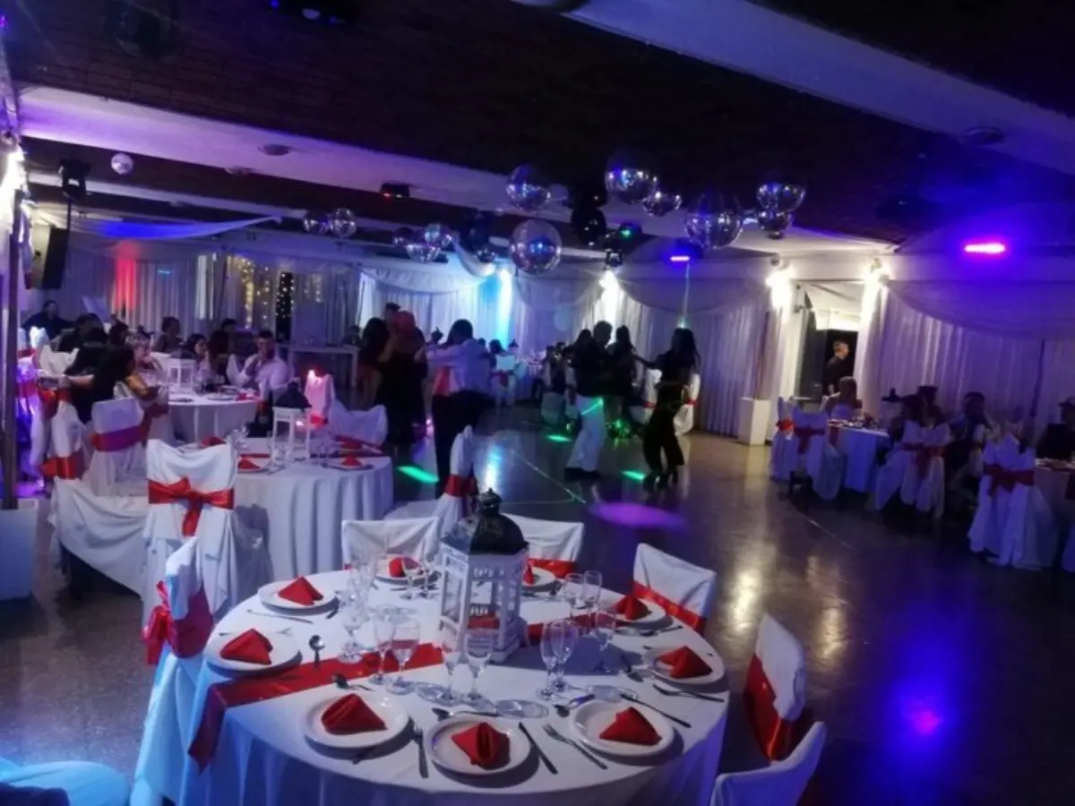 Fiesta en curso: invitados en las mesas con moños rojos y pista iluminada de fondo