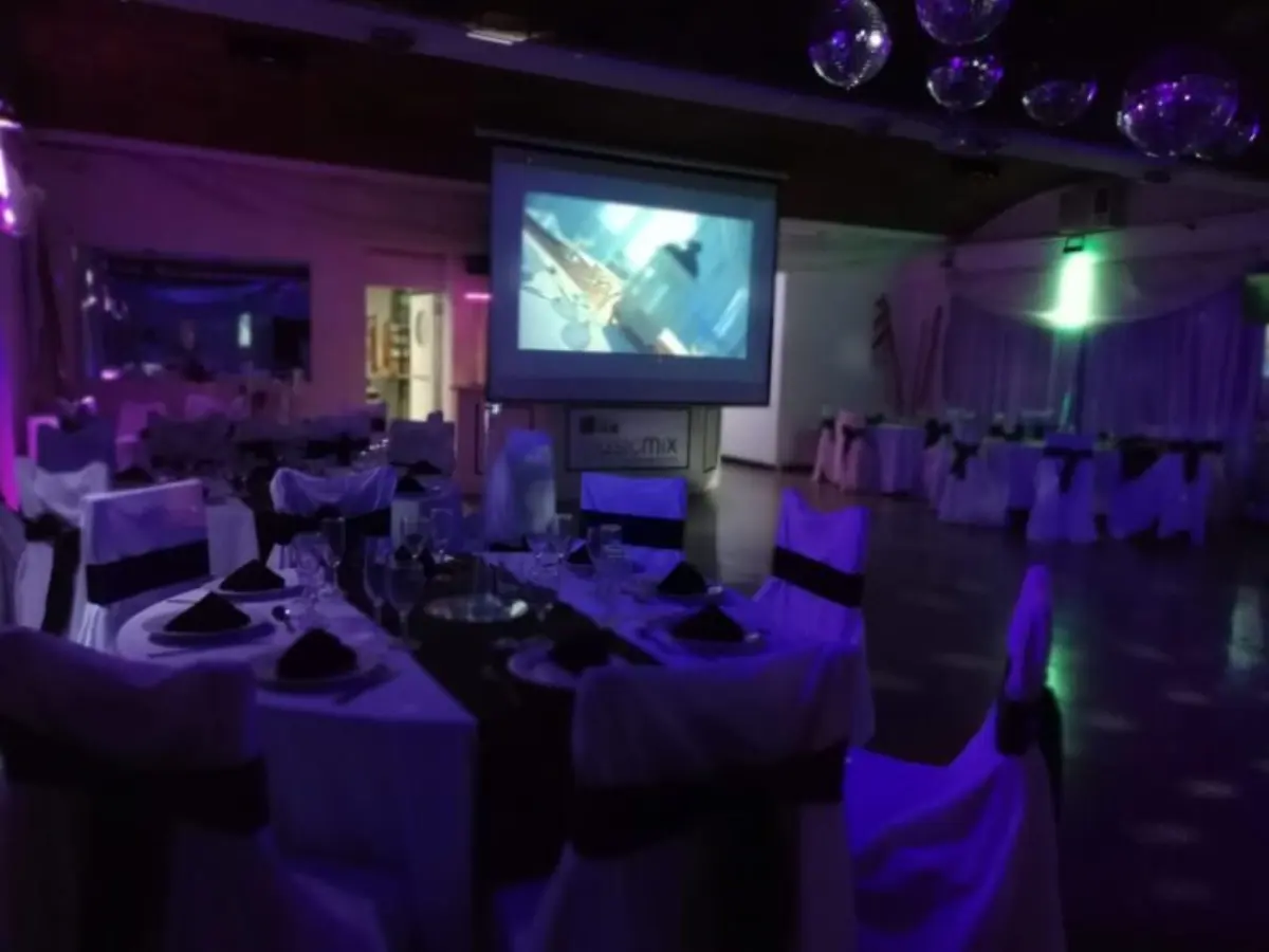 Mesa vestida con mantel negro frente a una pantalla, bajo luces violetas del salón