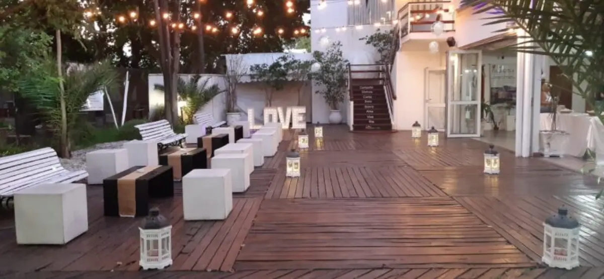 Deck al aire libre con guirnaldas de luces, puffs blancos, faroles y letras luminosas LOVE