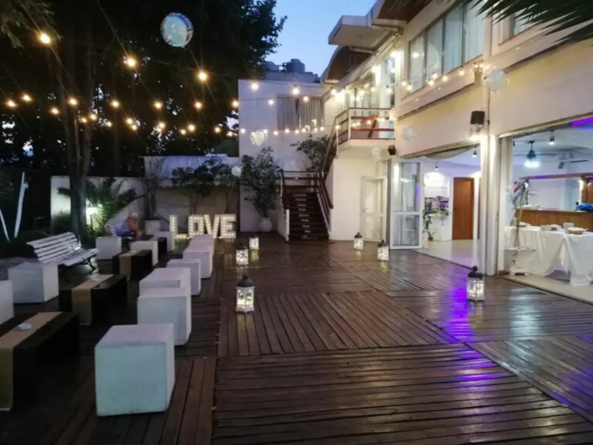 Deck exterior al atardecer con guirnaldas encendidas, puffs blancos y luces violetas en el piso