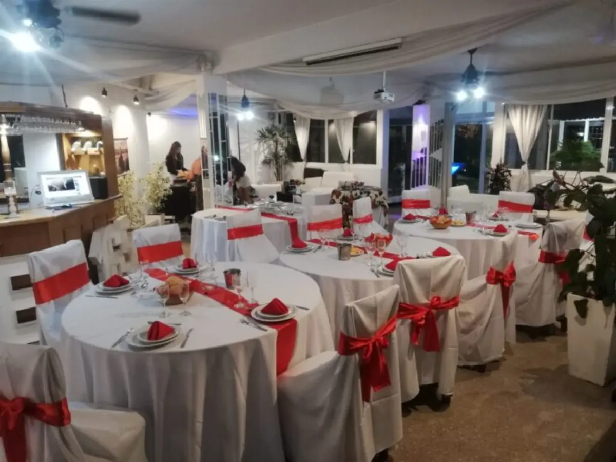 Salón montado con mesas redondas y moños rojos junto a los ventanales